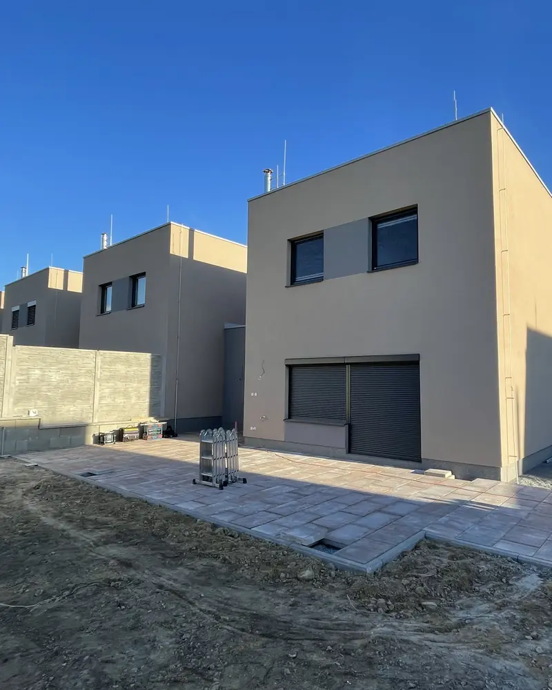Prázdná dlážděná terasa u novostavby, kolem hlína a stavební materiál.